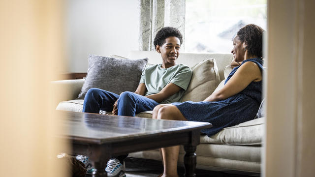 Single mother and teenage son having conversation on couch at home 