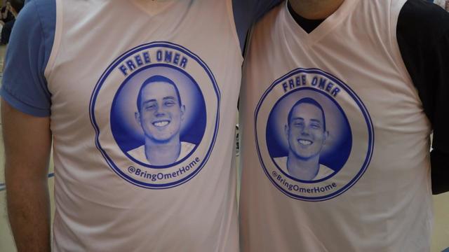 Two individuals wearing t-shirts that say "Free Omer" with a picture of Omer Neutra. 