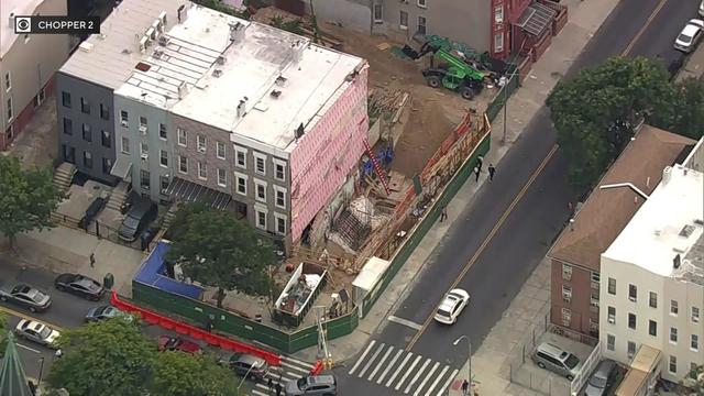 An aerial view of a construction site alongside a row of Brooklyn homes. 